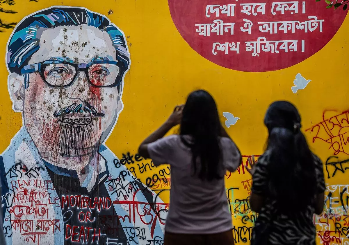 People take photos in front of anti-government graffitis on a vandalised mural depicting Bangladesh’s founding father Sheikh Mujibur Rahman days after a student-led uprising ended the 15-year rule of his daughter Sheikh Hasina in Dhaka on August 10.