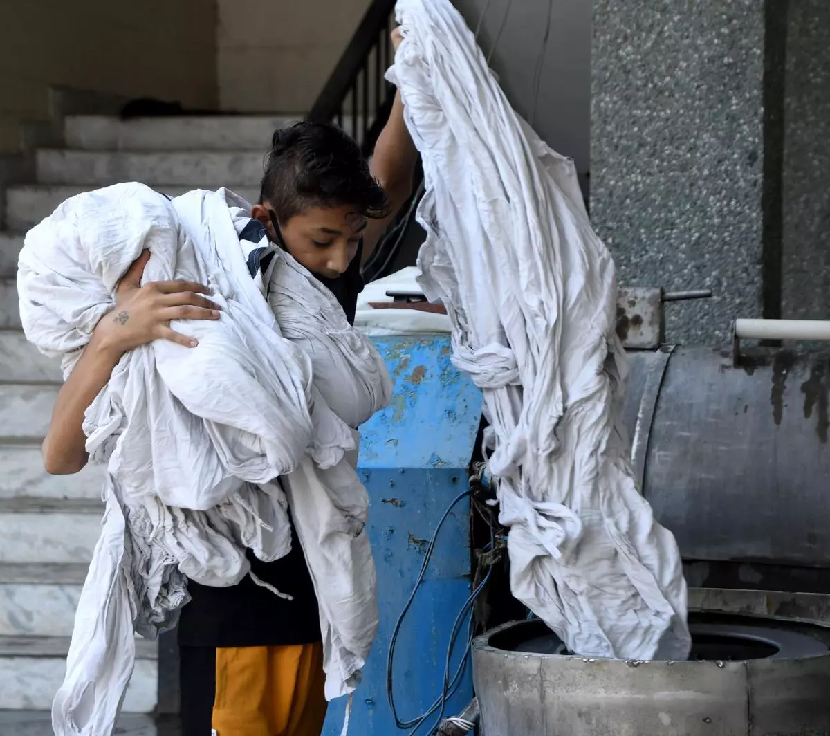 A washerman at the Vivek Vihar dhobi ghat carries hospital bedsheets during the pandemic. New Delhi, June 22, 2020. 