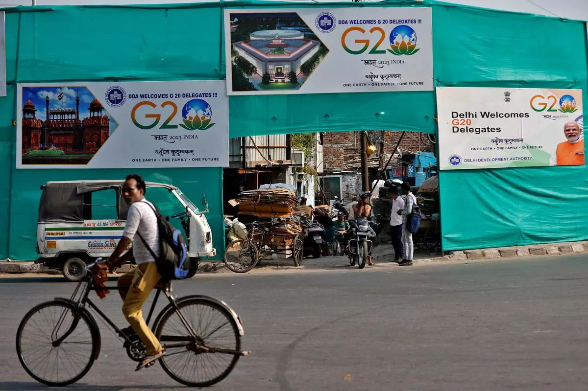 A man rides a bicycle past hoardings installed on plastic sheeting placed to screen a slum area alongside a road ahead of the G20 Summit in New Delhi.