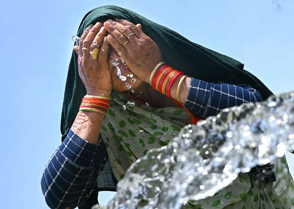 A woman washes her face with water to cool off during a hot summer day near the India Gate in New Delhi on June 17, 2024. 