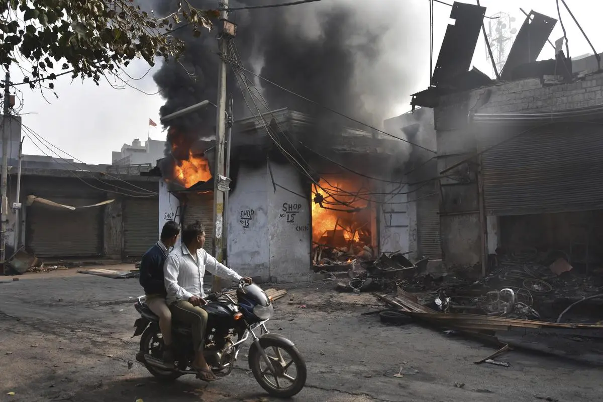 Two men drive past a shop that was set on fire by mobs during the protests against the Citizenship Amendment Act, in New Delhi on February 26, 2020.