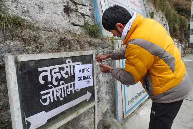 Local people paste placards with slogan ‘NTPC Go Back’ on a signboard as they protest against the project in landslide-hit Joshimath town of Chamoli district, Friday, Jan. 13, 2023. Local people paste placards with slogan ‘NTPC Go Back’ on a signboard as they protest against the project in landslide-hit Joshimath town of Chamoli district, Friday, Jan. 13, 2023.