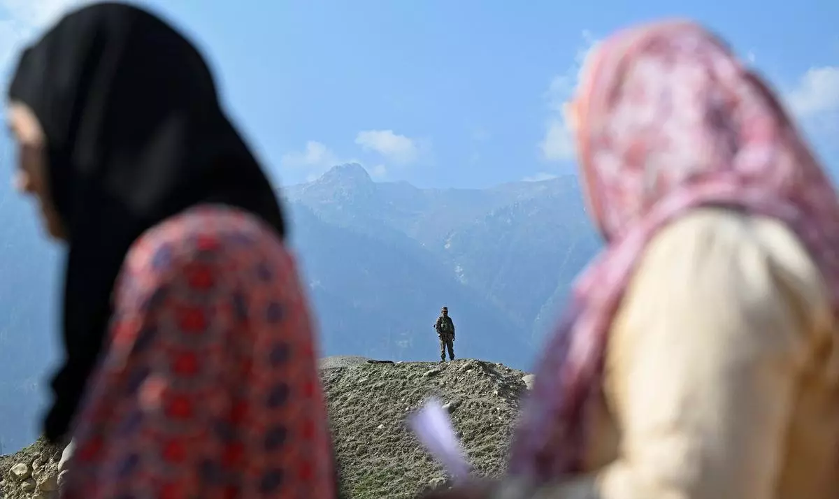 A security officer stands guard as voters line up to cast their ballots at a polling station during the second phase of Kashmir Assembly elections in Ganderbal on September 25, 2024. 