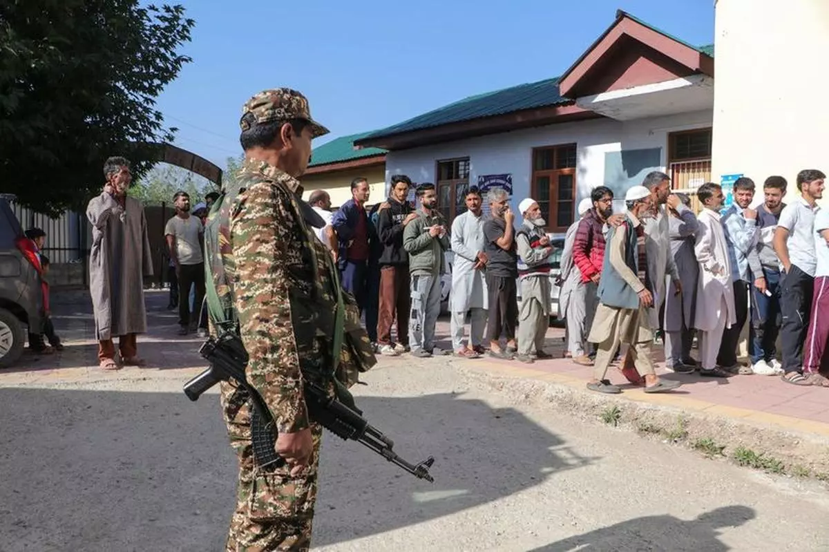 Army stands guard as people queue to cast their votes at a polling station during the final phase of the election in Baramulla on October 1, 2024.