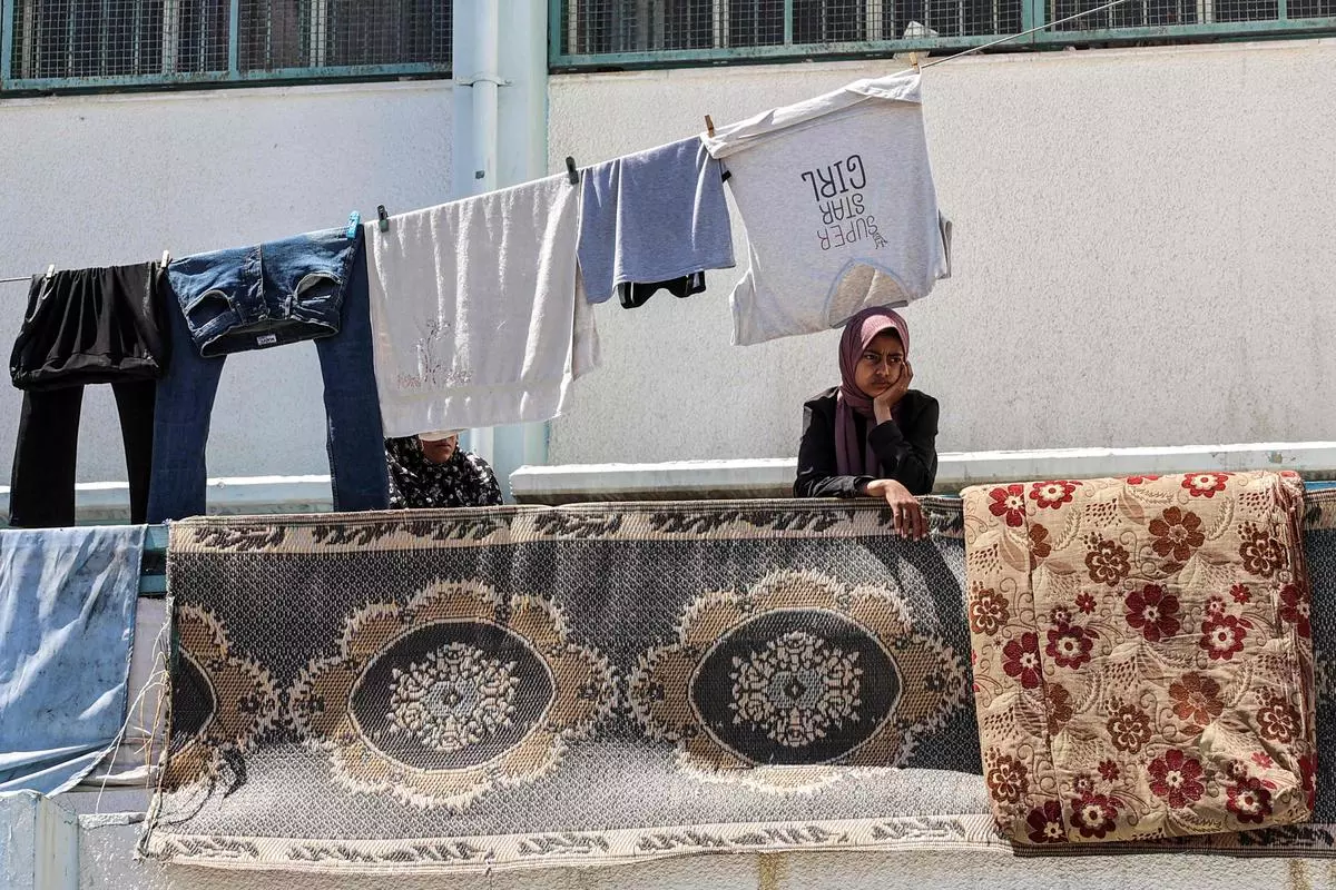 A girl stands beneath clothes drying on a laundry line at a school run by the United Nations Relief and Works Agency for Palestine Refugees in the Near East (UNRWA) at the Shati camp for Palestinian refugees, west of Gaza City, on May 7, 2024.