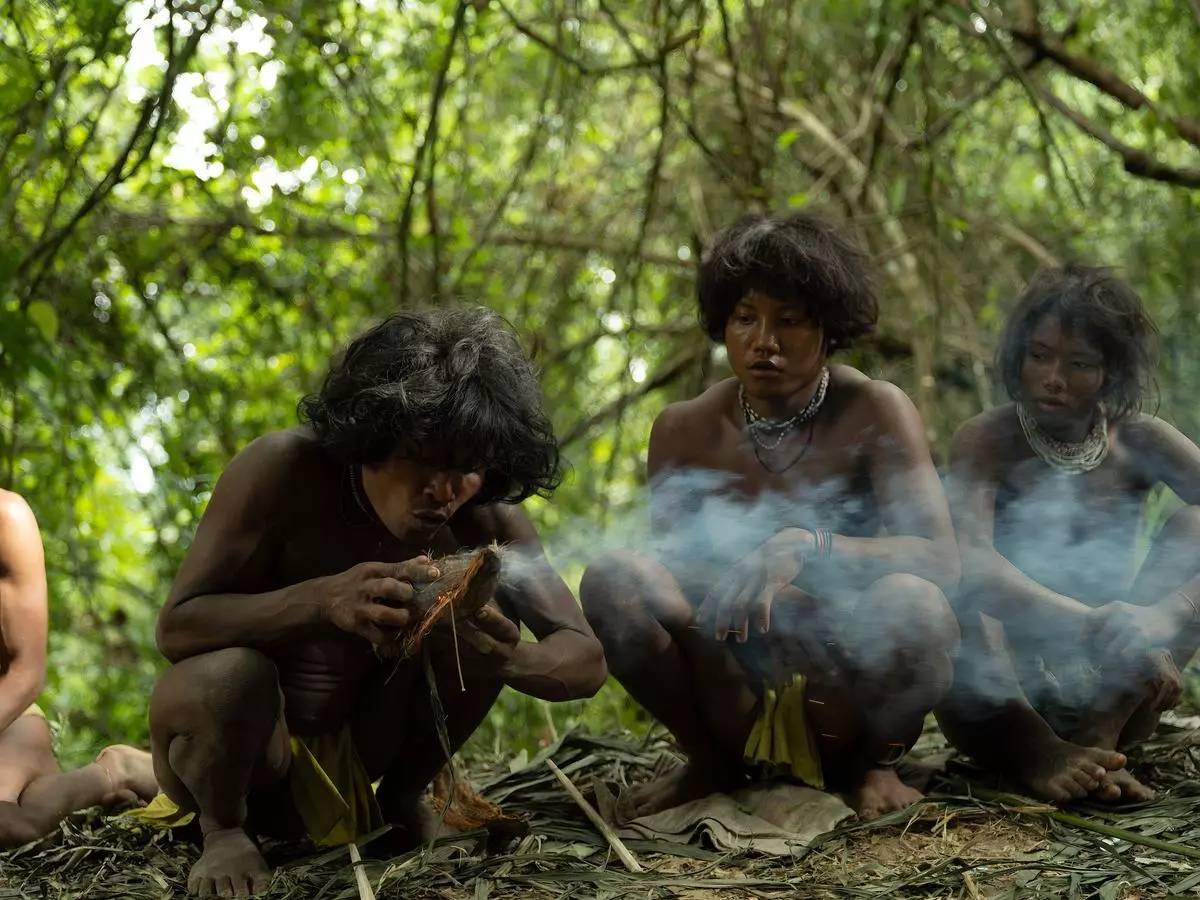 A Shompen man crouches low, blowing on a coconut husk to ignite a fire, while his companions watch intently.