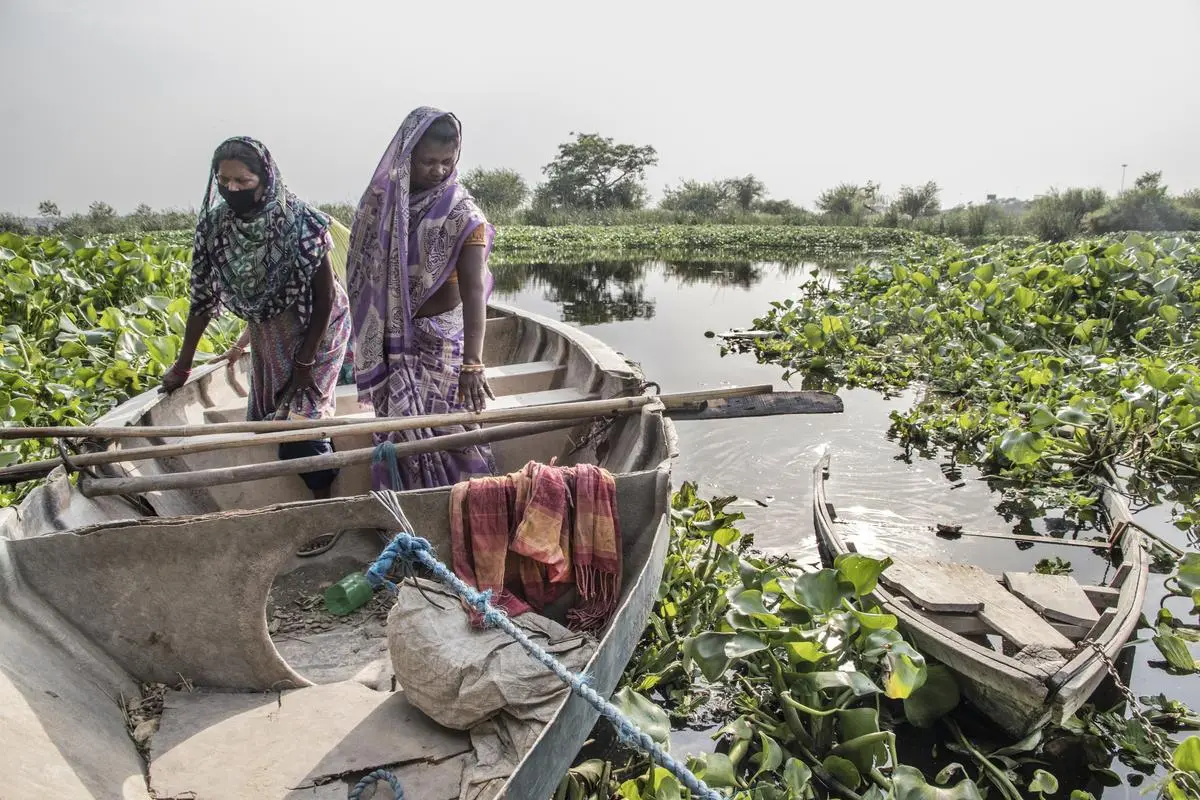 Bhudani Devi, 45 (right), alights from her boat at her doorstep. Her home is in the middle of the Yamuna riverbelt in Delhi. Bhudani and her family of 10 use boats to commute for work, fetch food, and to escape the rising waters. For nine years in a row, the family has been displaced by floods. Their condition was worsened during the pandemic. With one of their boats broken, they are now trying to make another with wood from the scrap market. If that fails, they will borrow the river guard’s discarded boat. Bhudani Devi, 45 (right), alights from her boat at her doorstep. Her home is in the middle of the Yamuna riverbelt in Delhi. Bhudani and her family of 10 use boats to commute for work, fetch food, and to escape the rising waters. For nine years in a row, the family has been displaced by floods. Their condition was worsened during the pandemic. With one of their boats broken, they are now trying to make another with wood from the scrap market. If that fails, they will borrow the river guard’s discarded boat.