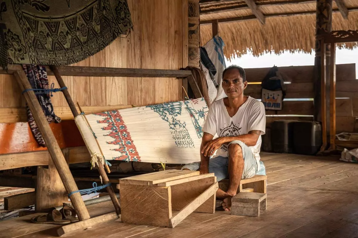 Umbu Nadwa poses for a photo while taping together individual threads. Historically reserved for women, the process of making Sumbanese fabric has been extended to men.