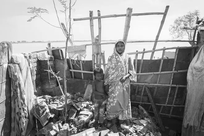 Juli Bibi, 33, and her son pose for a photo in a bamboo-enclosed makeshift shelter dangerously close to the progressing river. She lost her home to the Ganga in 2021.